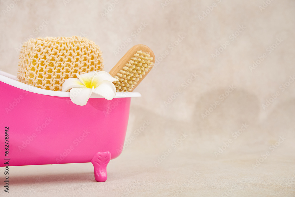 Small bathtub with sponge, massage brush and flower on light background