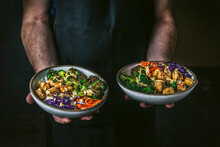 Man Holding 2 Bowls With Charred Vegetables And Tofu