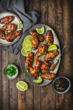 Glazed Chicken Wings Arranged On Metal Plate And Serving Plate With Limes, Sauce, And Scallions