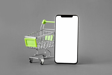 Shopping cart and mobile phone on grey background