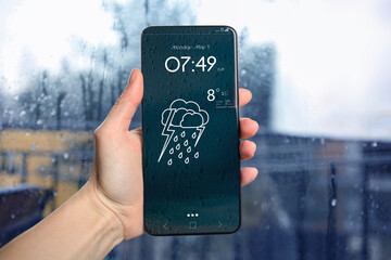 Wall Mural - woman checking weather using app on smartphone near wet window, closeup. data and illustration of cl