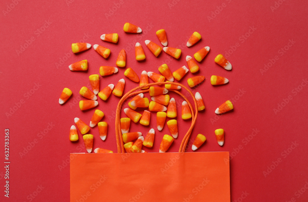 Shopping bag with tasty Halloween candy corns on red background