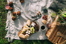 flatlay picnic scene with a basket and flowers, juice, grapes, cheese and a baguette