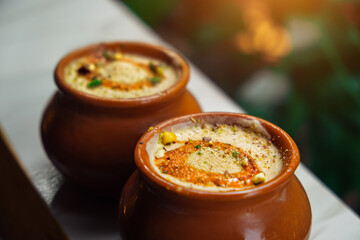 Kulfi or Qulfi ice cream in a clay pot. Kulfi is a popular traditional Indian dessert made of milk with spices and nuts. Two clay pots with ice cream on a blurry background