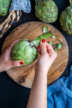 Woman Hands Removing The Outer Leaves Of An Artichoke.