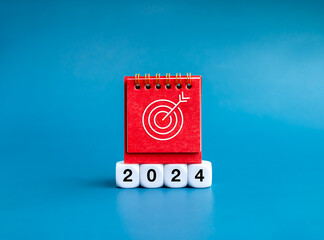 Poster - Happy new year 2024 with goals action plan banner background concept. Target icon on red desk calendar cover standing on white blocks with 2024 year numbers isolated on blue background, minimal style.