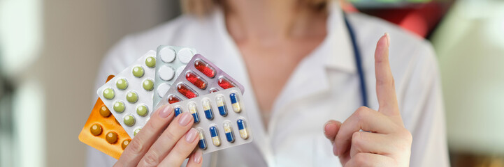 Wall Mural - Female pharmacist holds packs of medical pills and points her finger up.