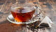© Uuganbayar - Glass transparent cup of black tea and dry tea in bags on the background of scattered tea leaves on the old wooden background, selective focus