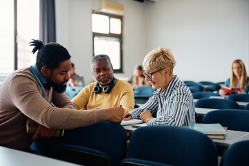 Mature students learning with help of African American teacher in lecture hall.