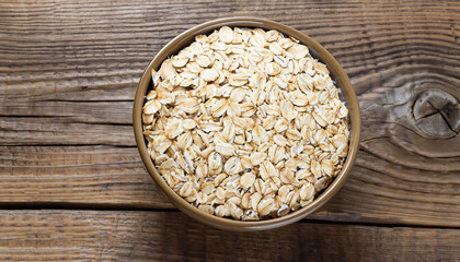 Wall Mural - Oat flakes in a round bowl on the old wooden background, top view