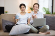 © SOMKID - Two roommates woman sitting on a sofa in the living room at home, Friendship and sisterhood concept.