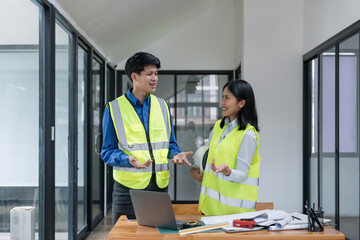 Wall Mural - Two young man and woman engineers meeting, working, discussing, planing, designing, measuring layout of building blueprints in construction site floor at factory