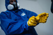 Mann säubert Gebäude von Asbest im blauen Schutzanzug mit gelben Handschuhen und einer Schutzmaske 