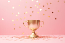 Golden Winners Cup With Flying Star Confetti On A Pastel Pink Background, Front View