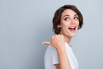 Photo of sweet excited woman dressed white t-shirt showing thumb back looking empty space isolated grey color background