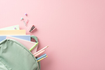 Schoolgirl's delight: Top view of open sage backpack with pencils, pens, notebooks, mini stapler, pushpins and clips for upcoming school season. Advertise in the pink pastel backdrop
