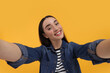 © New Africa - Smiling young woman taking selfie on yellow background