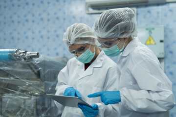 Two female worker inspecting quality of plastic water tank on conveyor belt in drinking water factory. Group of scientist using tablet working, checking bottle, gallon on conveyor production line