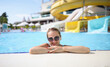 © H_Ko - Portrait of woman in sunglasses in water park in pool. Hotel services with concept water parks