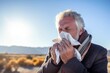 © Leon Waltz - Medium shot portrait photography of a man in his 50s sneezing and holding a tissue because of the flu wearing a foulard against a sky background