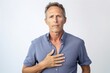© Leon Waltz - Medium shot portrait photography of a man in his 40s clutching his chest due to gastroesophageal reflux disease wearing a simple tunic against a white background