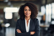 Mujer de raza negra con pelo rizado largo, ejecutiva de una empresa, con traje y brazos cruzados, con fondo desenfocado de una oficina