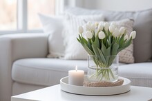 In A Scandinavian Style Home, There Is A Lovely Arrangement Of White Tulip Flowers In A Glass Vase, Accompanied By A Tray Holding Candles On Top Of A Wooden Cabinet. The Overall Design Is Minimalist