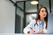 © bnenin - A serious female doctor taking notes on paper and looking at the laptop screen.