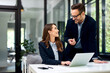 © bnenin - Male and female employees talking at the office while a woman typing on a laptop.