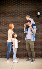 Wall Mural - Family with a mother, father, son and daughter standing by the wall of brick house