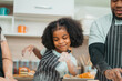 © chokniti - Kind African american parents teaching their adorable daughter how to cook healthy food, free space of kitchen, Happy black people family preparing healthy food in kitchen together