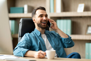 Aufkleber - Smiling Young Businessman Talking On Cellphone And Drinking Coffee At Workplace