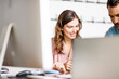 © Connect Images - Smiling young businesswoman listening to colleague at desk in office