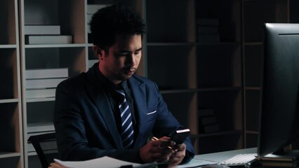 Poster - Tired young Asian businessman working overtime in the office room at night, trying to get things done before the deadline.