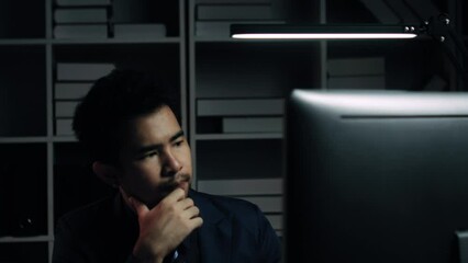 Poster - Tired young Asian businessman working overtime in the office room at night, trying to get things done before the deadline.
