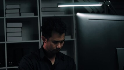 Poster - Tired young Asian businessman working overtime in the office room at night, trying to get things done before the deadline.