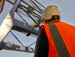© Connect Images - Low angle view of dock worker beneath crane at Port of Felixstowe, England