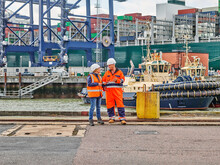 Dock Workers Standing Infront Of Tug And Cargo Container Ship On Digital Tablet