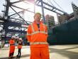 © Connect Images - Low angle portrait of dock worker wearing reflective clothing in dockyard, Felixstowe, England.