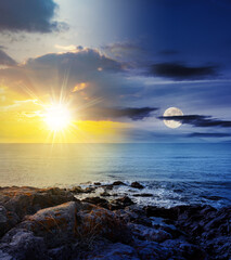 Wall Mural - sea wave attacks the boulders of rocky shore with sun and moon at twilight. day and night time chang