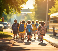Group Of Children Walking On The Sidewalk In A Street With Backpacks, Back To School, Schoolbus In Blurred Background
