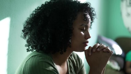 Wall Mural - A hopeful Brazilian young woman praying at home. An African South American person having FAITH