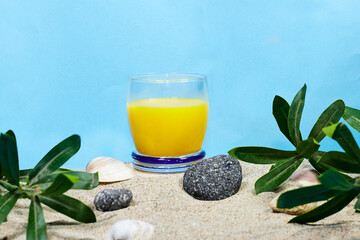 Glass of 100% Orange juice on sand with stones and plants. summer concept 