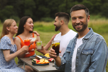 Canvas Print - Friends having cocktail party outdoors. Happy man with glass of drink, selective focus