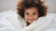 
A Very Cute Little Black African Baby Kid With Afro Hair Wrapped In Soft White Blanket On A Bed Smiling. Image Perfect For Ads. Big Beautiful Eyes And Tiny Nose,