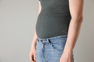 Wall Mural - Overweight man in tight tshirt and jeans on light grey background, closeup. Space for text