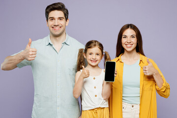 Wall Mural - Young parents mom dad with child kid girl 6 years old wearing blue yellow casual clothes hold use blank screen mobile cell phone show thumb up isolated on plain purple background. Family day concept.