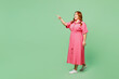 Full body side view young chubby redhead woman wears casual clothes pink dress point index finger aside on area while walking isolated on plain pastel light green color background. Lifesyle concept.