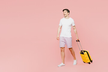 Poster - Traveler side view man wear summer casual clothes hold suitcase walk go isolated on plain pink background studio. Tourist travel abroad in free spare time rest getaway Air flight trip journey concept