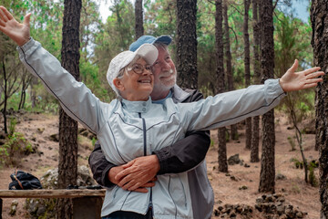 Wall Mural - Happy senior couple hugging enjoying mountain hike in the woods appreciating nature and freedom, retired seniors man and woman and healthy lifestyle concept